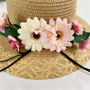 Close-up of hand-woven straw sun hat with pink daisy flowers and delicate black cord