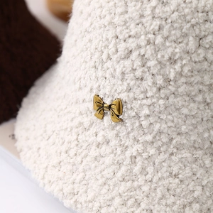 Detail of soft cream plush bucket hat featuring a decorative gold bow metal buckle