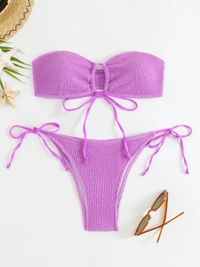 Flat lay of purple bandeau bikini with textured fabric, seashells and summer accessories