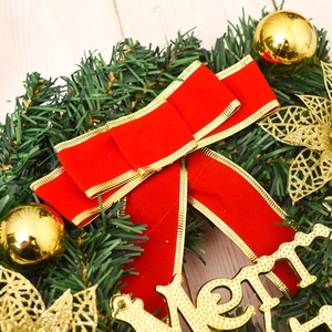 Close-up of a Christmas wreath with a red velvet bow and golden ornaments on wood