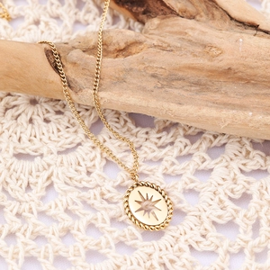 Close-up of golden necklace featuring an oval starburst pendant with woven edges