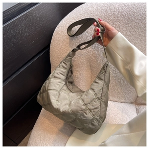 Detailed view of sage green quilted nylon crescent bag held by model on white plush chair