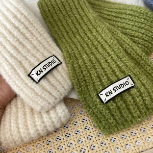 Close-up of soft ribbed knit texture on cream and green scarves with KN STUDIO label
