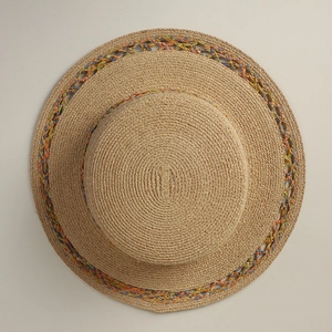 Top view of a wide-brim raffia hat featuring colorful hollow knit patterns on the brim