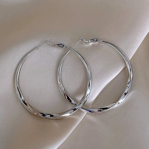 Elegant large silver twisted hoop earrings displayed on champagne silk fabric background