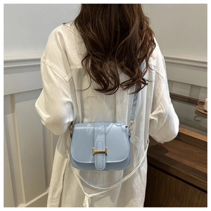 Close-up of light blue saddle bag with golden H clasp on model in a minimalist room