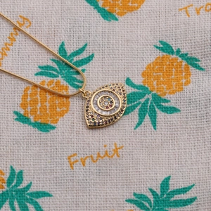 Detail of gold evil eye necklace pendant set with colorful zircons on summer fabric