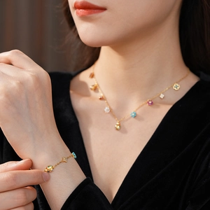 Detailed close-up of gold necklace and bracelet with enamel flower and ladybug charms