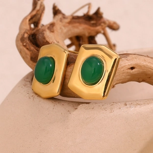 Close-up of gold geometric earrings with green oval stone on a rustic branch