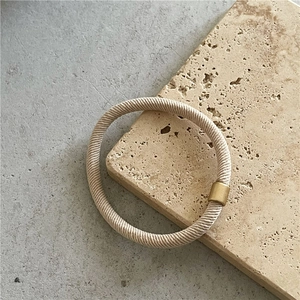 Detail of high-elastic beige hair tie with a matte gold metal cylinder fastener