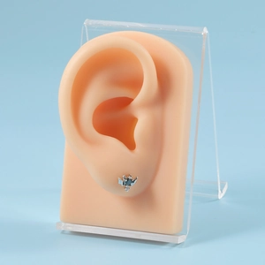 Detailed view of silver wing-shaped stud earring with dark blue zircon on a silicone ear