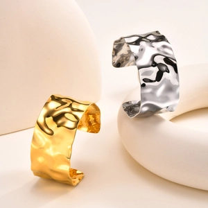 Detail of gold and silver C-shaped open bracelets with hammered texture on beige props