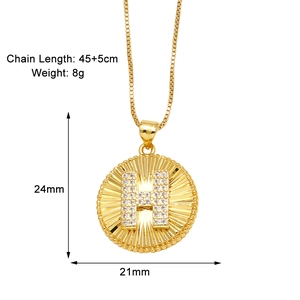 Macro di una collana con ciondolo a moneta d'oro con lettera H in cristallo e perline