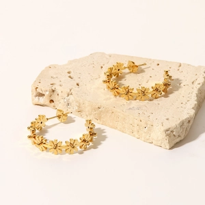 Detalle de pendientes de aro con flor en titanio chapado en oro 18K sobre base piedra