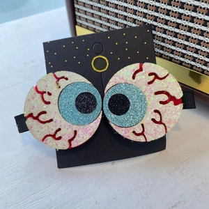 Barrette Halloween œil scintillant avec veines rouges sur carte de présentation noire