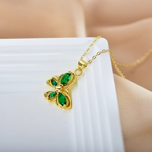 Macro detail of gold butterfly pendant with green gemstone inlay on delicate chain