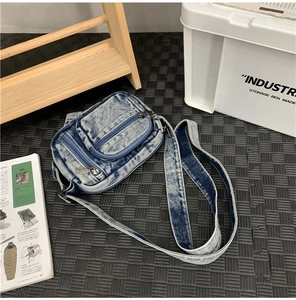 Detailed flat lay of a vintage washed denim crossbody bag with metal zippers and wide strap