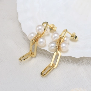 Macro view of gold chain link earrings with natural white pearls on white shell background