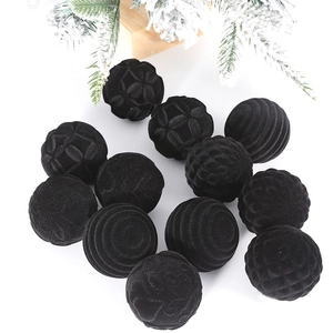 Close-up of 12 black flocked Christmas balls with textured patterns and snowy pine needles