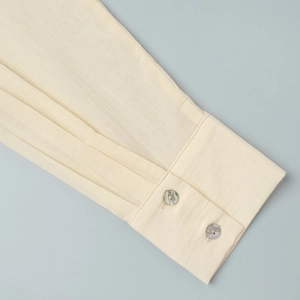 Detail shot of pleated sleeve cuffs on a cream woven shirt with pearl-like buttons