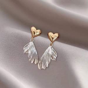 Detailed shot of gold heart studs with silver fan pendants on soft grey satin