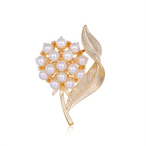 Détail d'une broche dorée en forme de fleur et feuille avec perles sur fond blanc