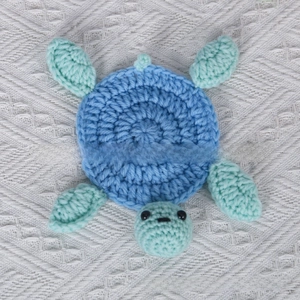 Macro detail of a handmade crochet turtle coaster featuring a blue and green spiral shell