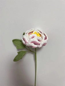 Close-up of handmade pink and white crocheted peony flower with green leaves