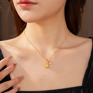 Dettaglio collana dorata con ciondolo a sfera cava e croce con pavé di diamanti brillanti