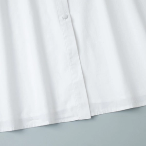 Gros plan sur l'ourlet de la robe blanche et les boutons recouverts en coton uni