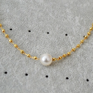 Macro detail of white pearl and faceted gold beads on a delicate brass necklace