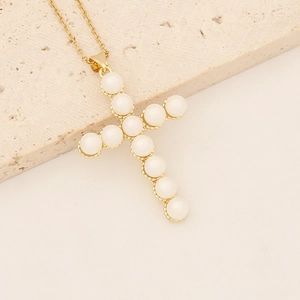 Golden cross necklace with white pearls and micro-pave cubic zirconia on stone background