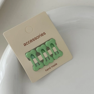 Close-up of three mint green bone-shaped metal hair clips with cute polka dot patterns