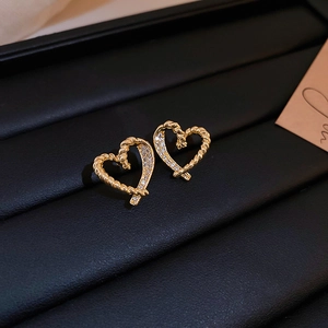 Detailed macro view of heart-shaped gold twist earrings with inlaid crystals on black leather