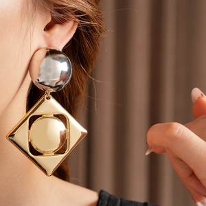 Close-up of geometric two-tone metal earrings with silver sphere and gold square pendant