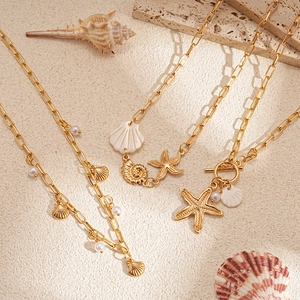 Detail of gold starfish and seashell charms on layered pearl and paperclip necklaces