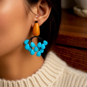 Close-up of orange and blue teardrop tassel earrings worn by a model in a knit sweater