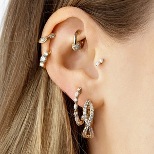 Macro shot of gold geometric zircon stud earrings and ear cuffs on a model's ear