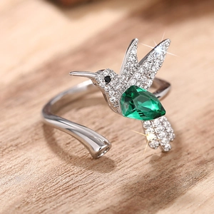 Detailopname van kolibrie ring met groene edelsteen en kristallen op licht hout