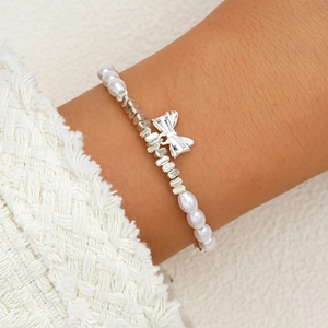 Elegant pearl bracelet with a silver bow pendant on a woman's wrist in a stylish view