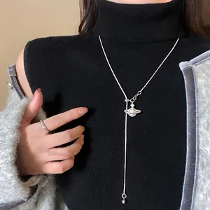 Détail du collier pendentif Saturne argenté avec perles sur fond de pull noir élégant