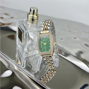 Detail shot of a tonneau emerald green watch with diamonds next to a perfume bottle