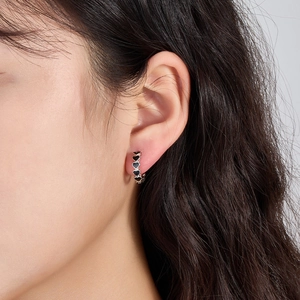 Close-up of 925 silver hoop earring with continuous black enamel heart pattern on model