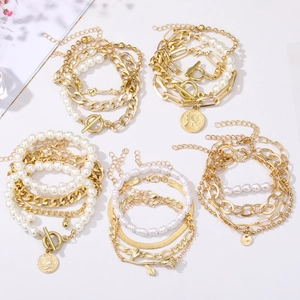Detail of layered gold metal chains with white pearls and coin charms on white background