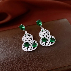 Macro shot of silver gourd earrings with green gems and intricate hollow filigree details