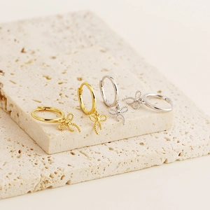 Detailed display of silver and gold bow earrings on elegant beige stone textures