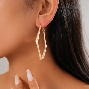 Close-up of a gold geometric rhombus hoop earring worn on a model's ear