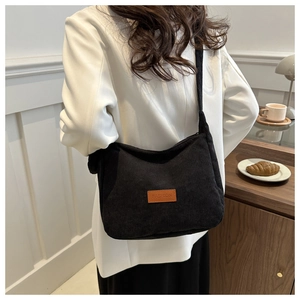 Detail of black corduroy shoulder bag with Fashion leather patch worn by model