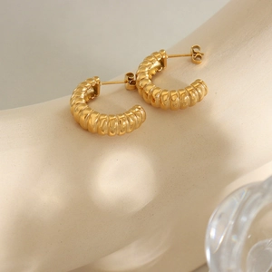 Golden C-shaped hoop earrings with spiral threaded texture on a minimalist background