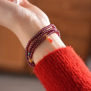 Detailed view of multi-layer garnet bracelet with golden gourd charm and amber beads
